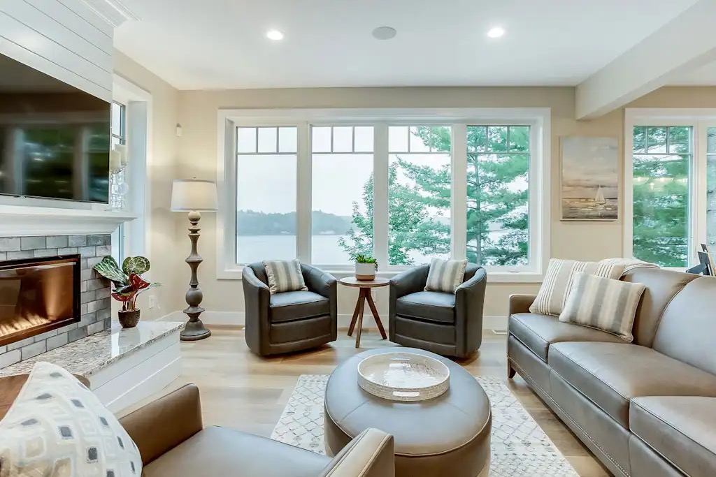 A lakehouse living room at Lakemore: lit fireplace, armchairs, and a wall of windows onto Arbutus Lake.
