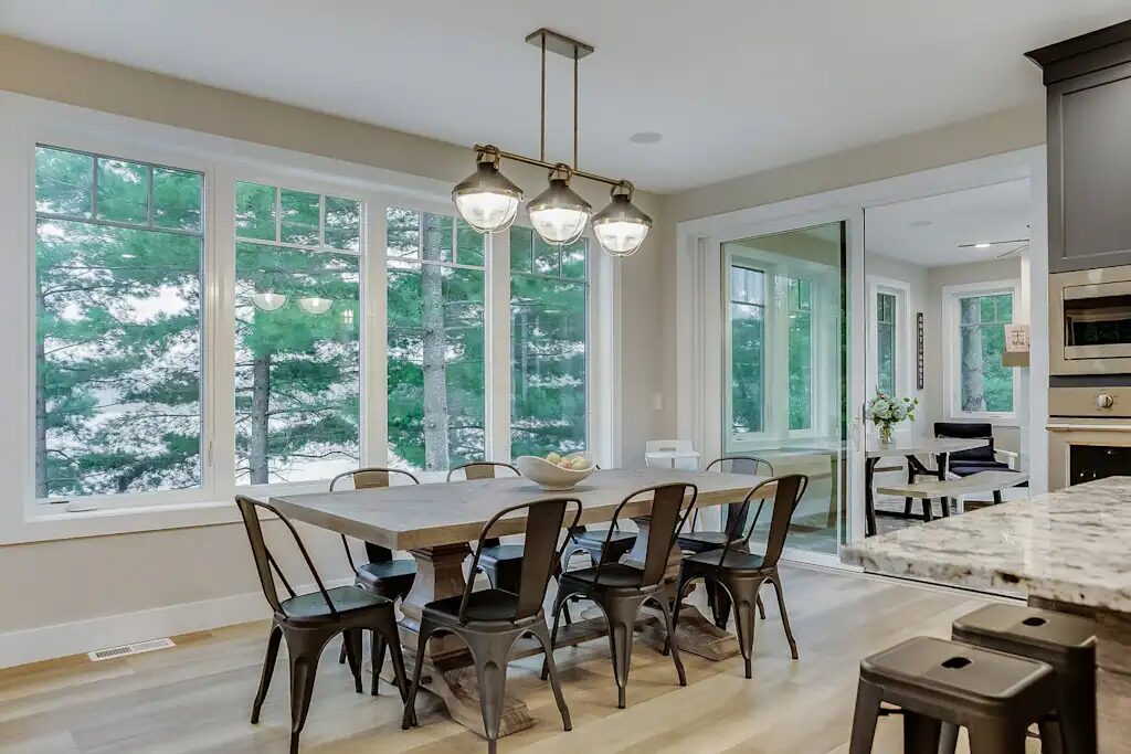A long dining table for eight beside a wall of windows looking into snowy pines.