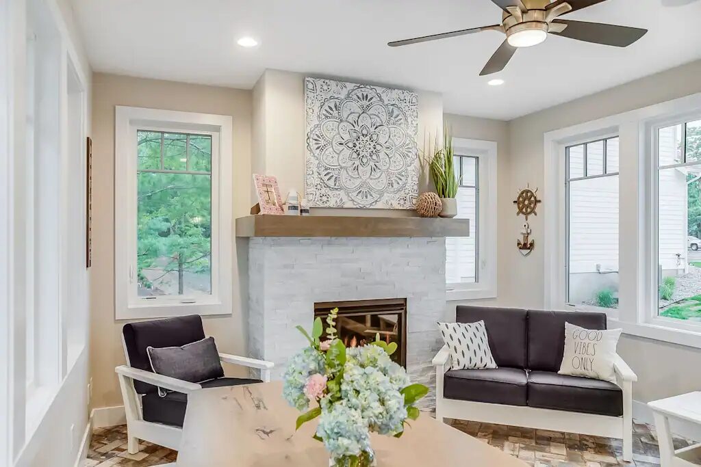 A bright sitting room with a stone fireplace, two settees and windows on both sides.